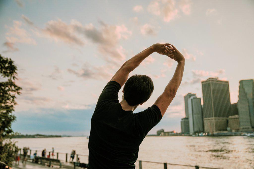 Male athlete stretching on waterfront during sunset.