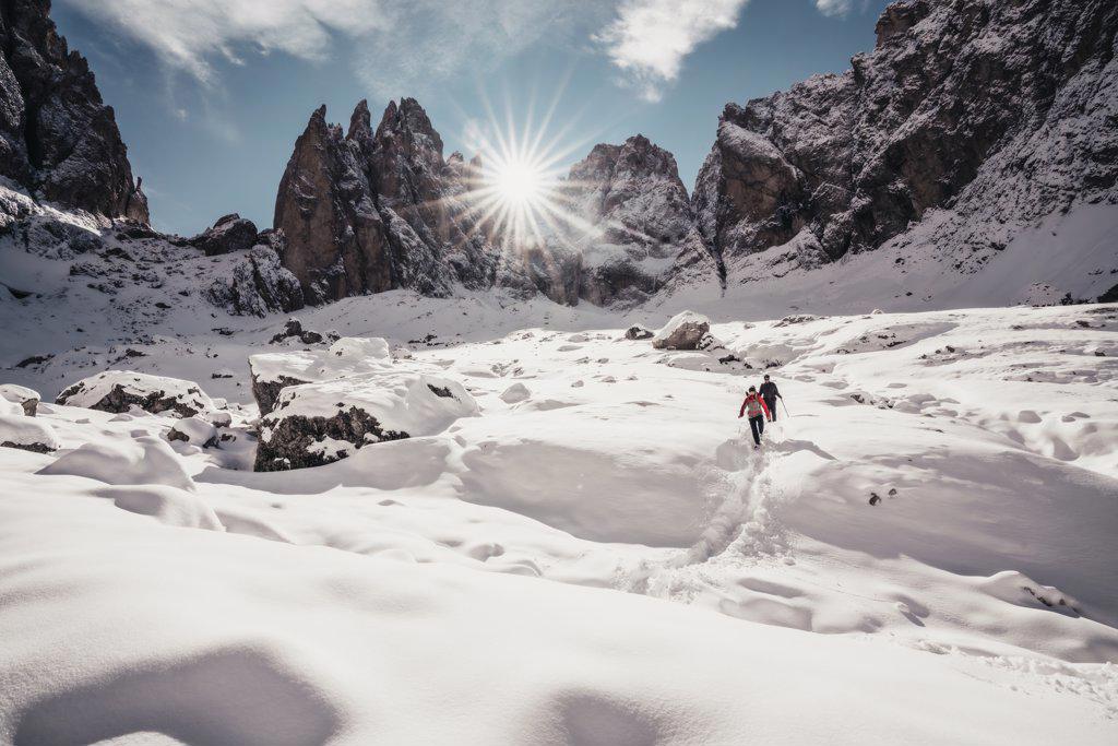 Two alpinists descending on snowy trail against sun rays in Dolomites