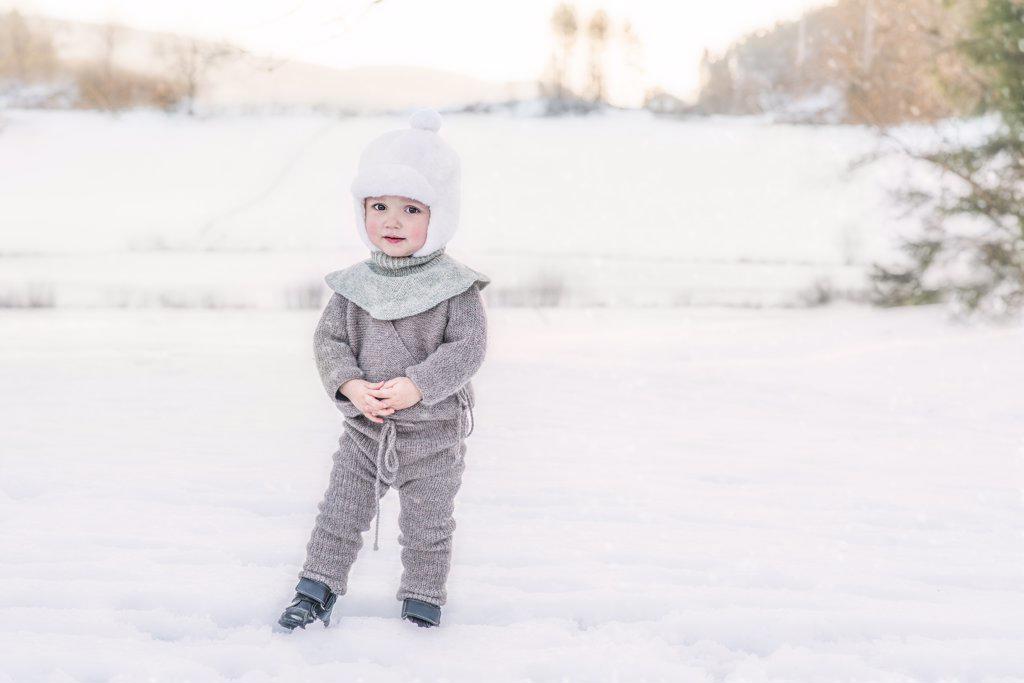 Adorable child standing in snow at farm wearing wool knitted clothes