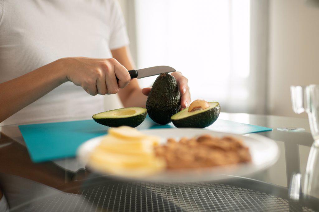 Crop woman cutting ripe avocado at table