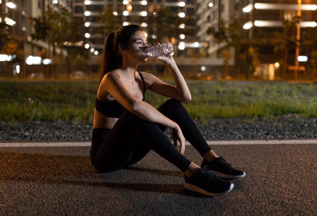 Sportswoman drinking water on track at night