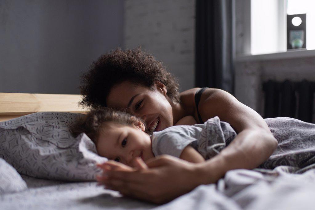 Cheerful mixed race mother and daughter lying on bed in morning