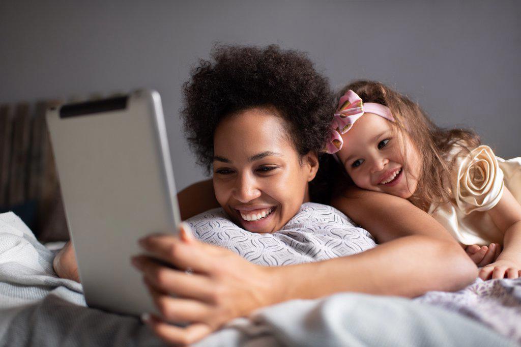 Mixed race mother and daughter making video call on bed