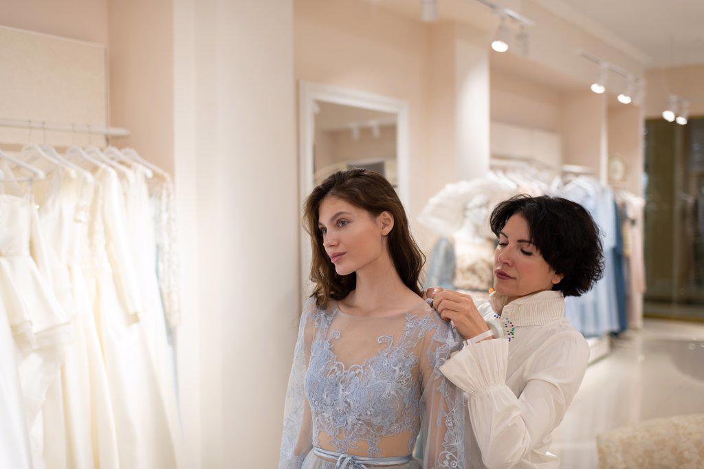 Young woman trying on dress with assistance of atelier owner