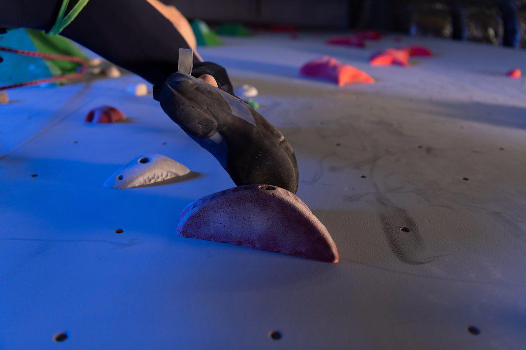 Cropped boulderer climbing wall in gym