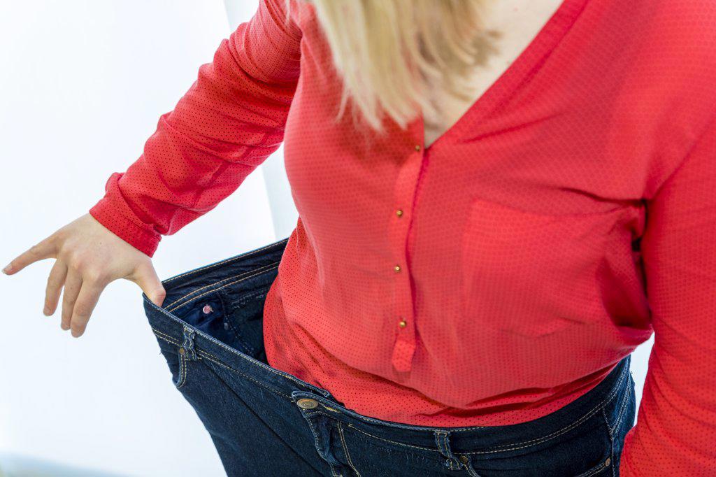 a young woman shows successher weight loss with her pants on