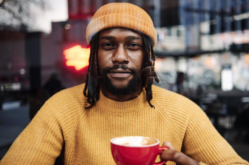 african male holding a cup of coffee while staring at the camera, reflection of the city on window