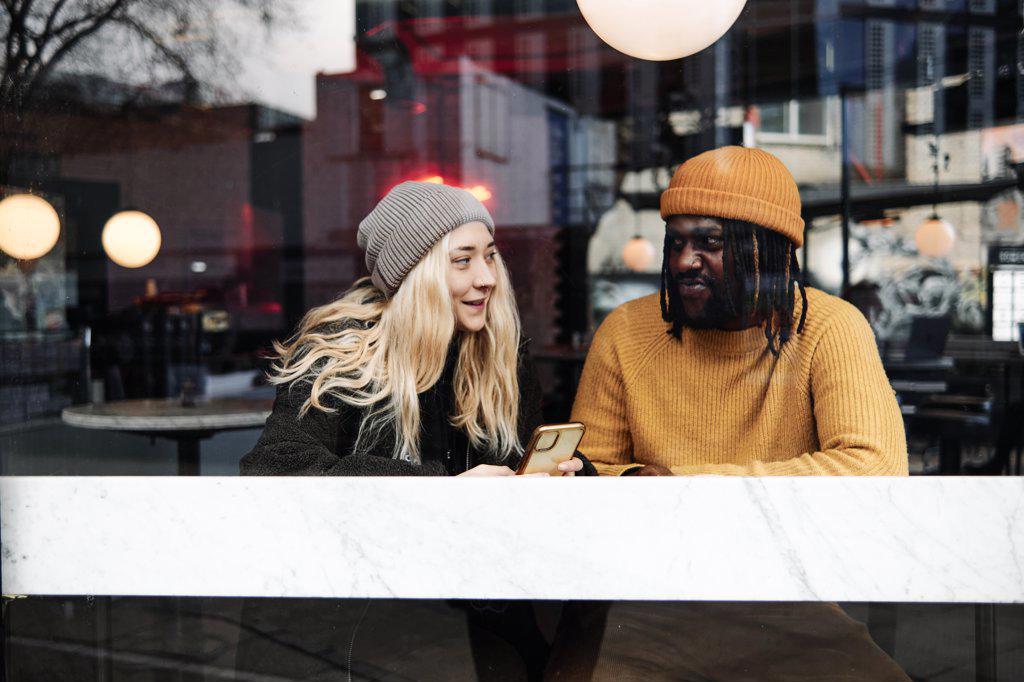 young biracial couple talking at the window of a cafe, reflection of the city on the glass