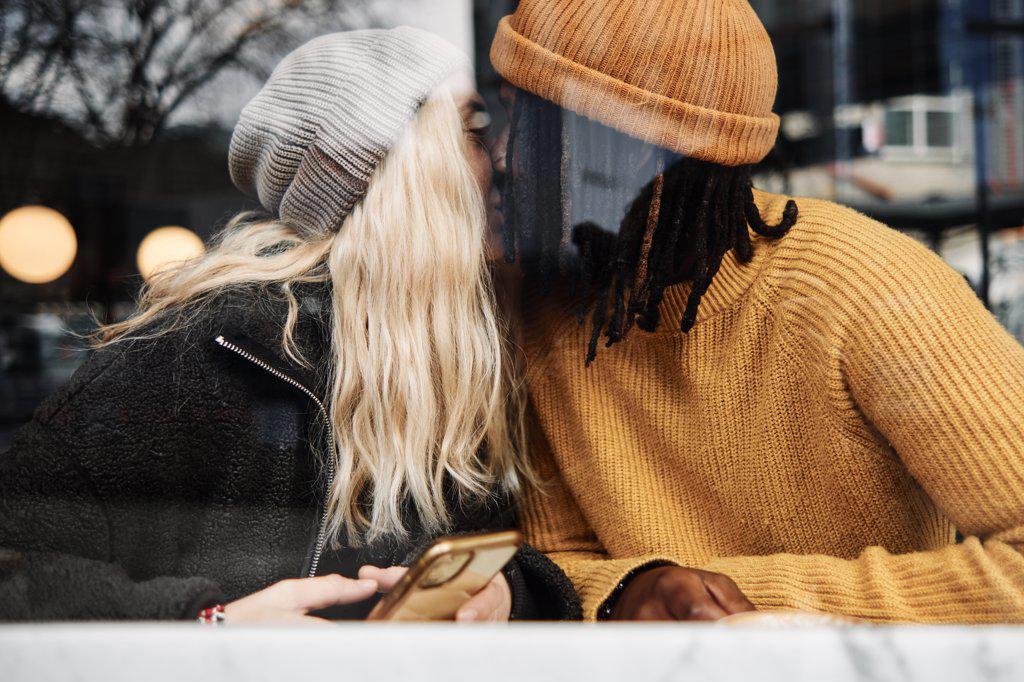 happy biracial couple kissing at the window of a cafe, reflection on the glass