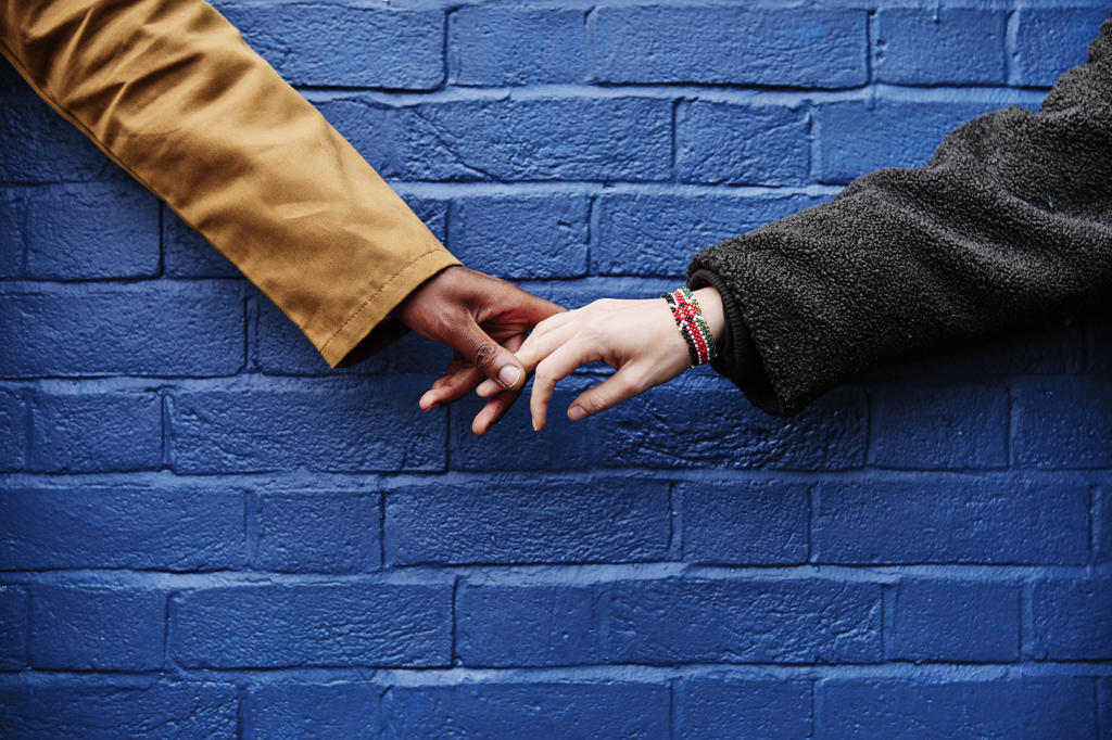 interracial couple holding hands, blue wall background. love symbolic concept.