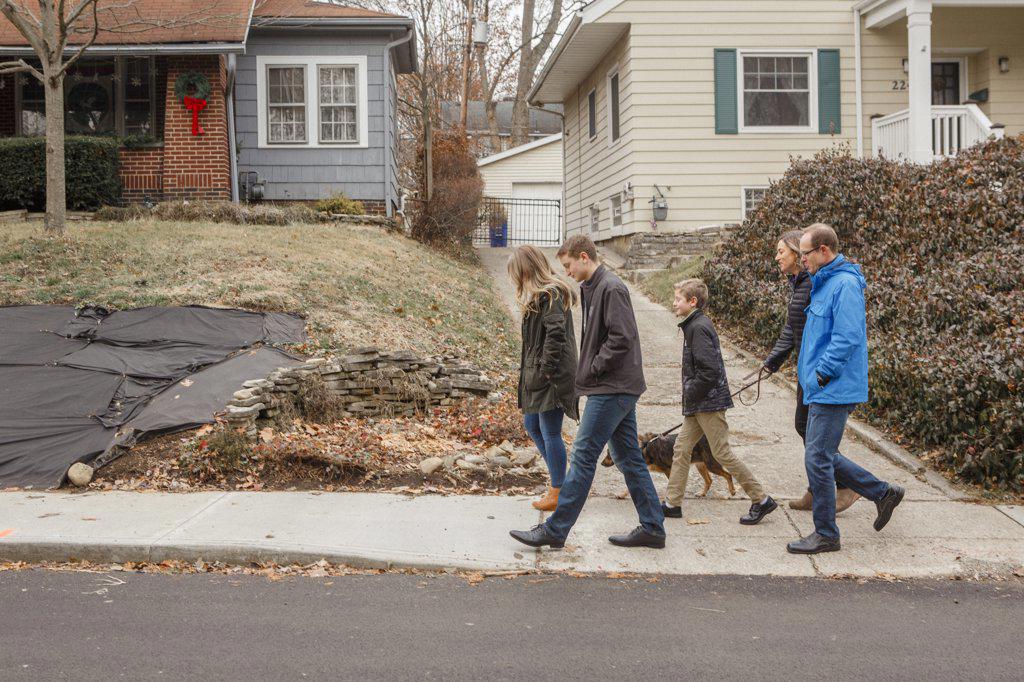 A family walk together with dog through suburban neighborhood