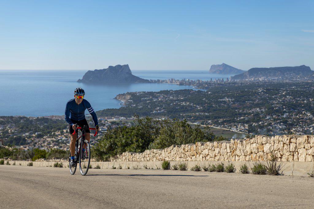 Cyclist climbing Cumbre del Sol hill with view of mediterranean sea.