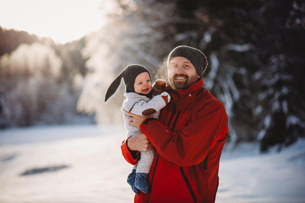 Father and baby smiling in winter wonderland full of snow in the woods