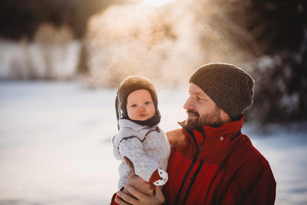 Dad and beautiful baby outside in snow in winter during golden sunset