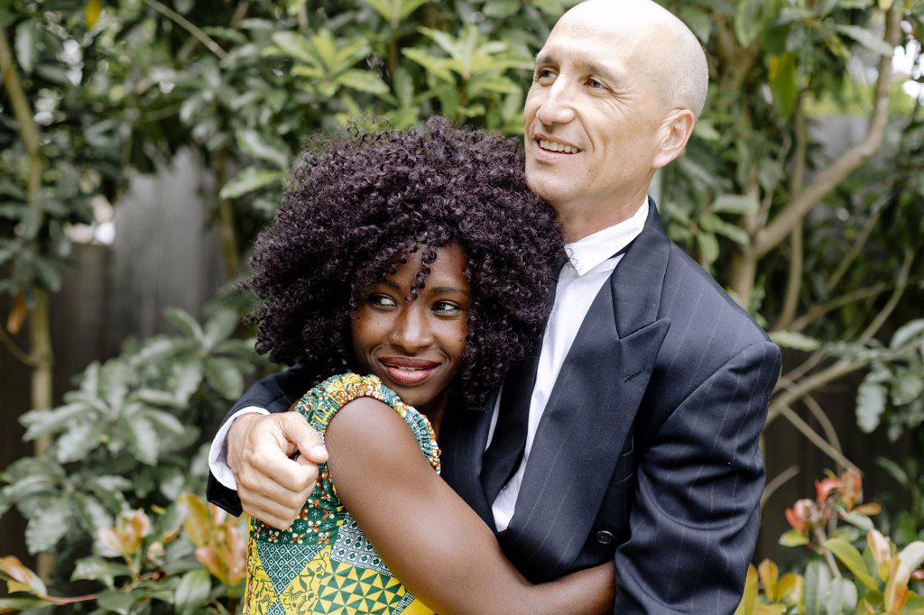 Interracial affectionate happy couple hugging  by garden
