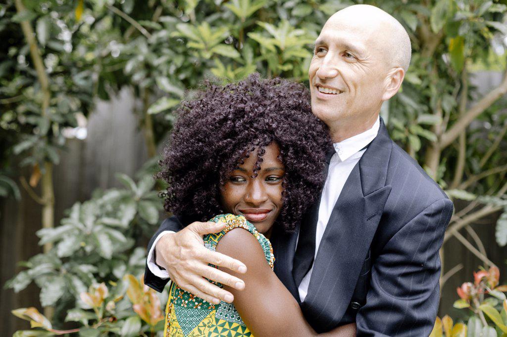 Interracial affectionate happy couple hugging by garden
