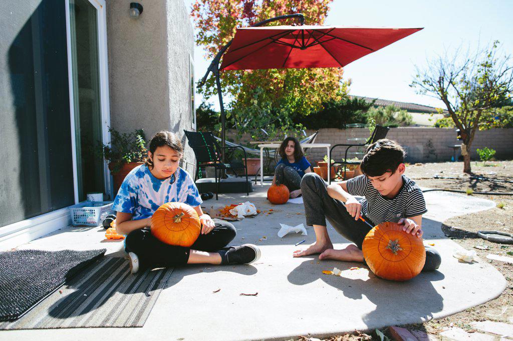 Three Kids Sit Outside and Carve Pumpkins
