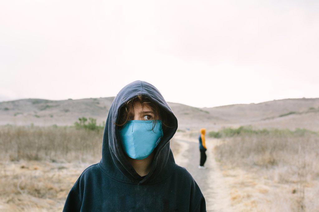 Teen Girl Wearing A Hoodie and Blue Face Mask Stands On a Nature Trail