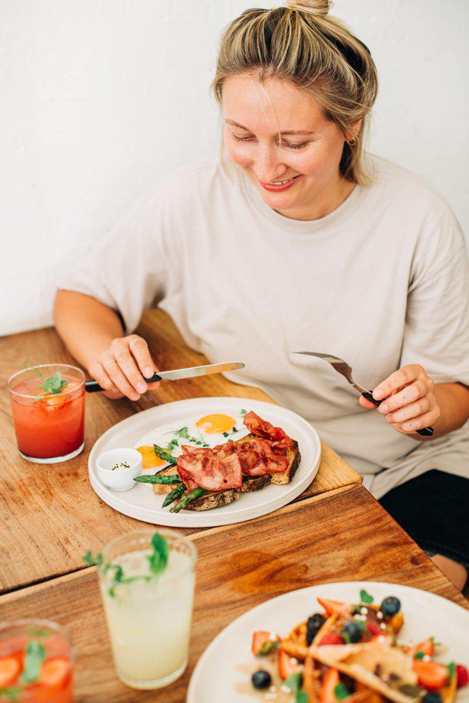 Woman eating fried eggs with bacon for breakfast