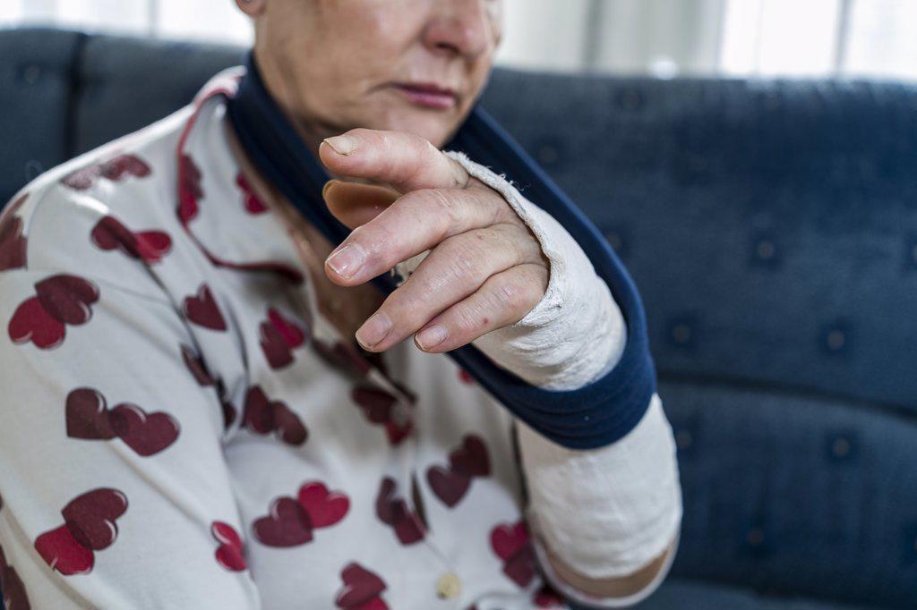 Caucasian senior woman with white hair with broken arm, sitting sofa