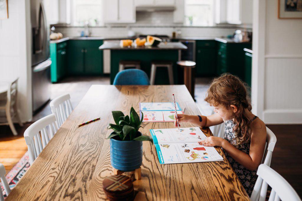 Young girl sitting at dining room table practicing school work