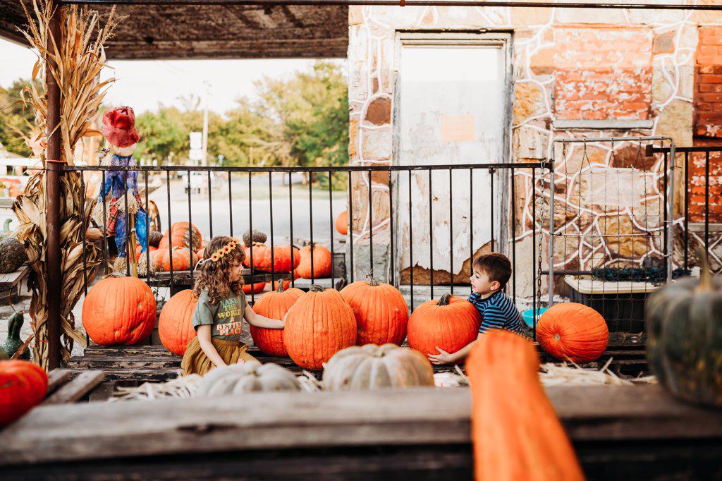 Brother and sister sitting surrounded by pumpkins at outdoor market