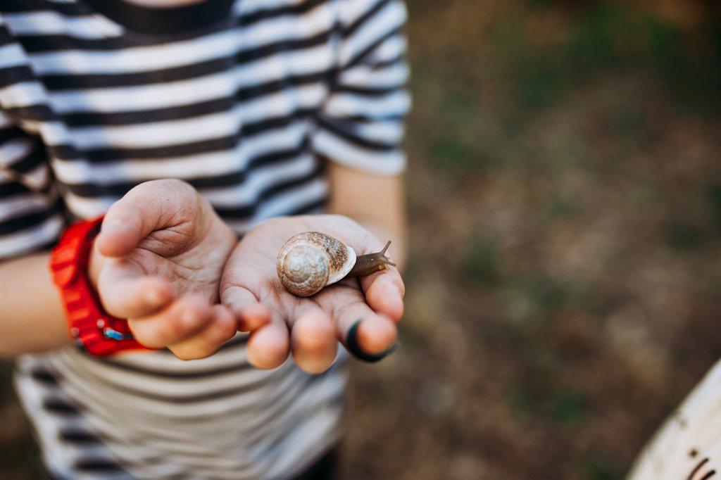 Close up of young boy outside holding snail in dirty hands