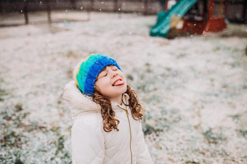 Young girl standing outside catching falling snow on tongue