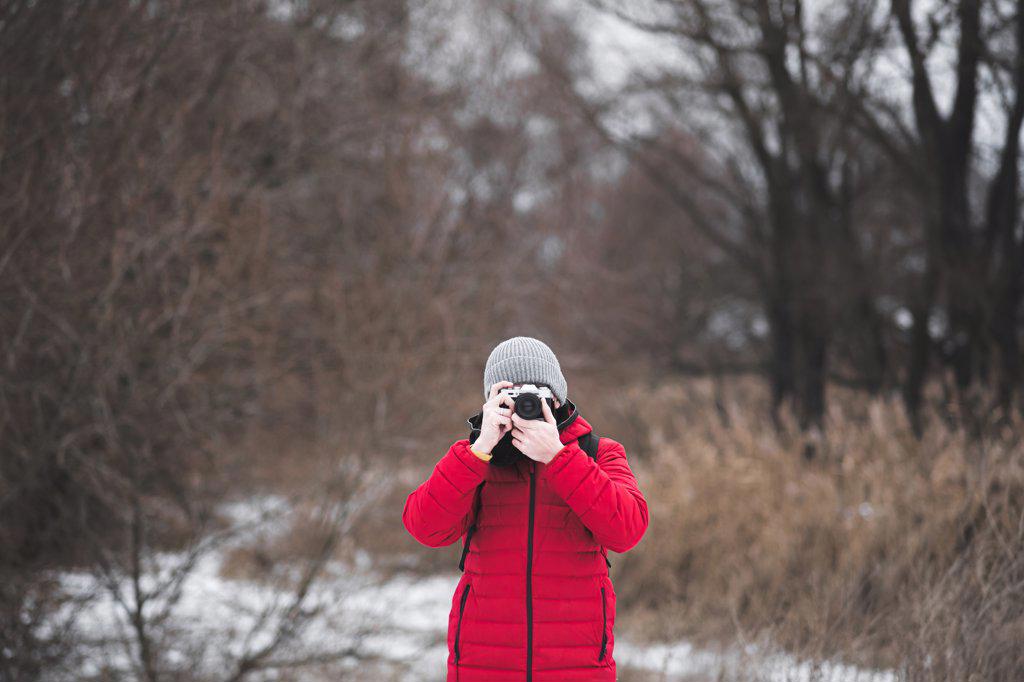 Man in red winter coat taking a picture in winter nature.