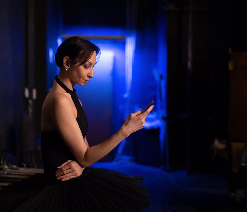 Ballerina using smartphone behind stage