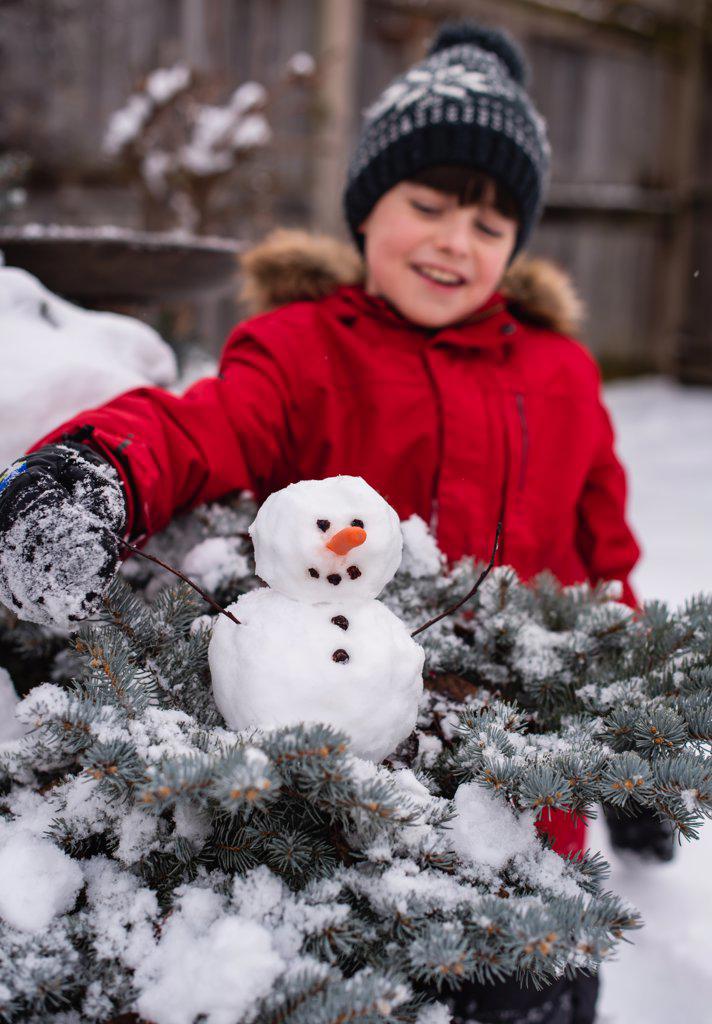 Boy looking at a small snowman on a shrub outdoors on a snowy day.