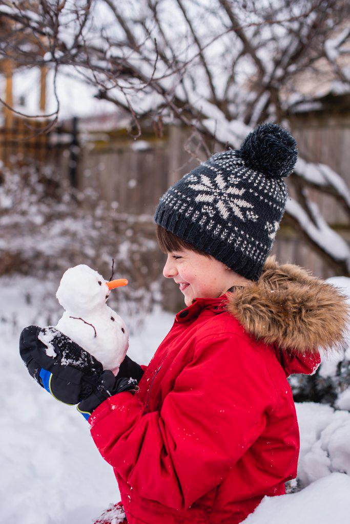 Boy holding a small snowman in his hands outdoors on a snowy day.