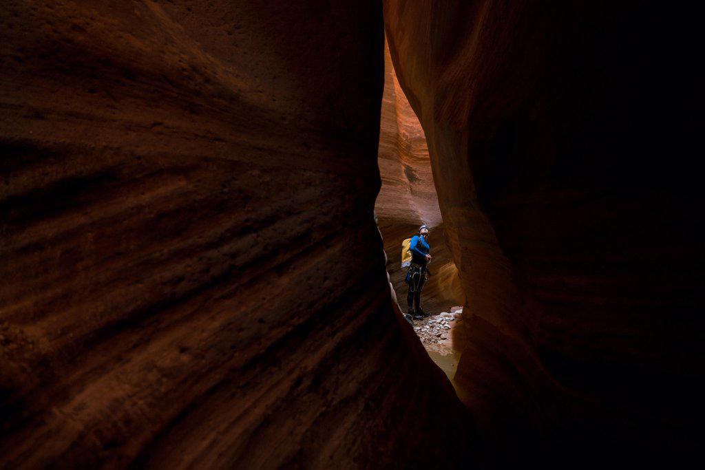 A man is seen through a small slit of red rock inside a canyon