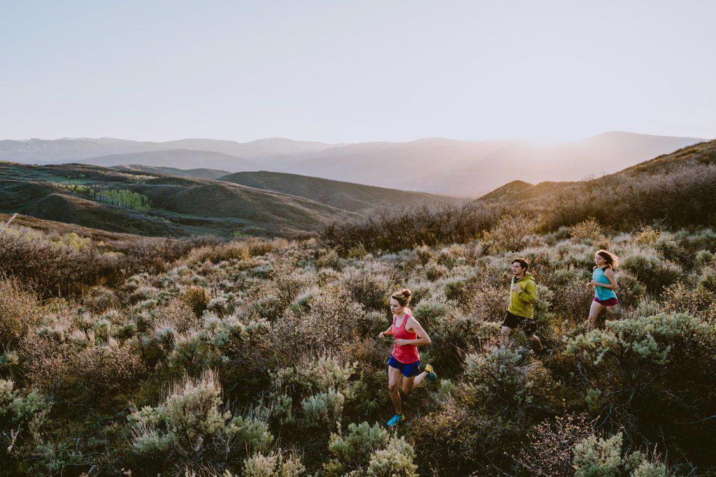 Three friends trail running in the mountains at golden hour