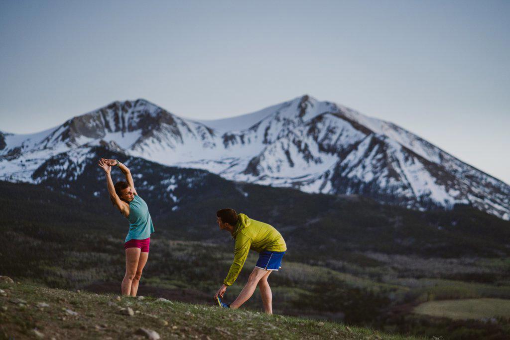 Two friends stretch before trail running with large mountains in view