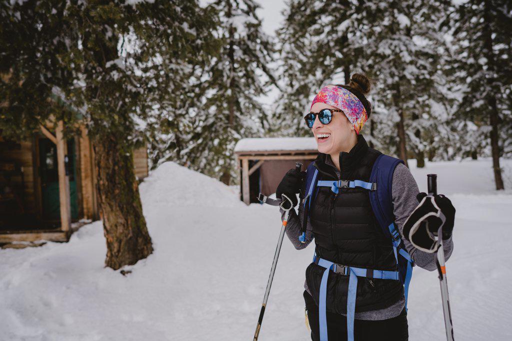 A woman with sunglasses and puffy laughs while XC skiing at cabin