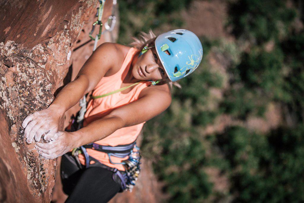 Female climber grasps onto rocks with chalked hands high on the wall
