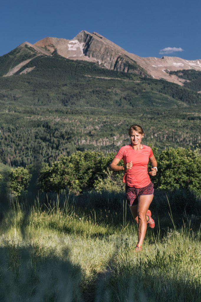 Athletic woman trail runs through grassy field with epic mountain view