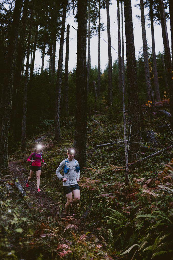 Two trail runners run down steep slope at night with headlamps glowing