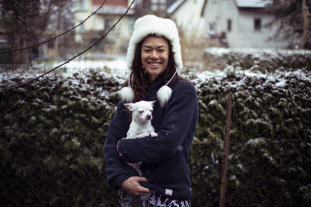 Asian woman smiles to camera white white fluffy hat and white dog dog