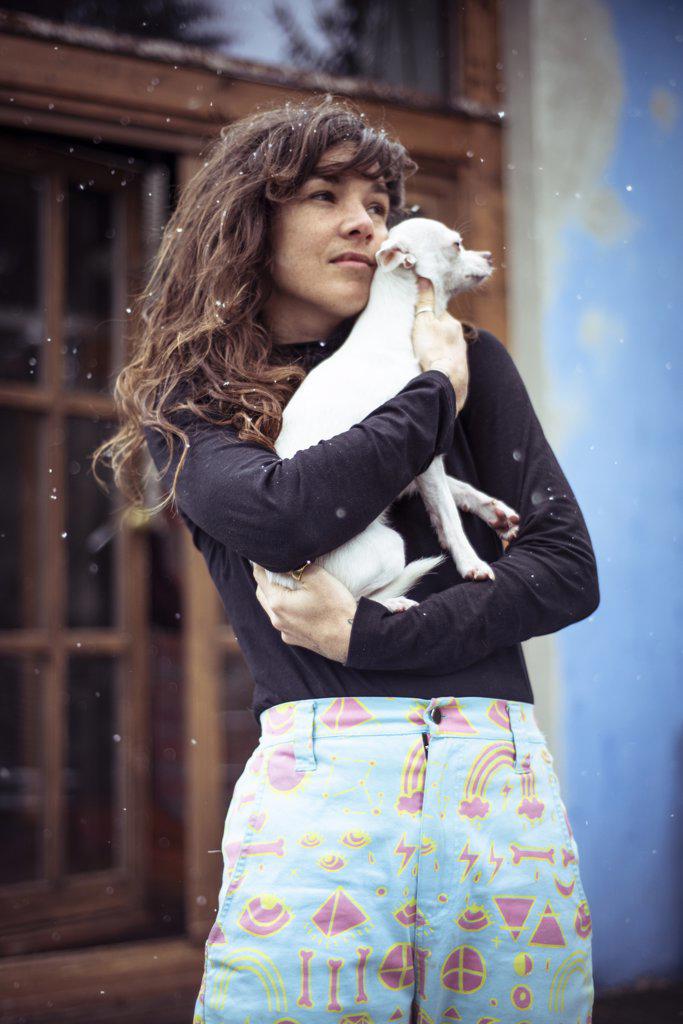 Woman with snow in hair holds small white dog to stay warm outside
