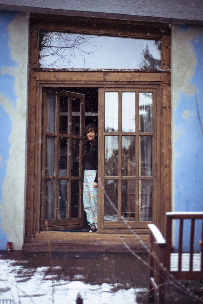 Woman with long curly hair & bright blue pants stands at wood doorway