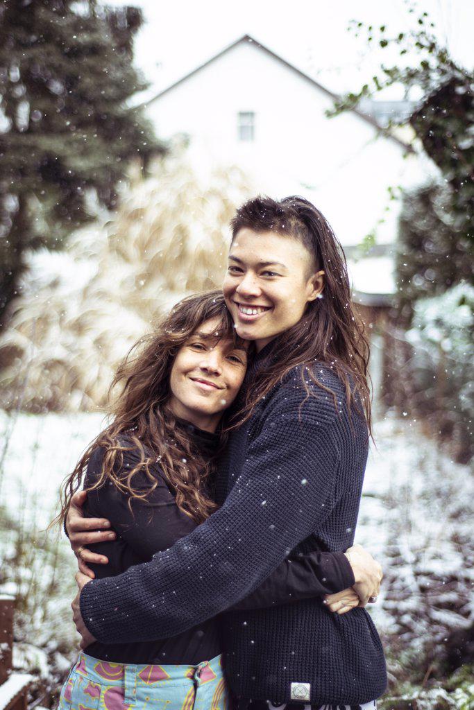 mixed-race queer women couple hug and smile in snow in europe winter