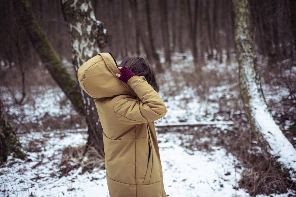 person puts hood on winter coat outside in snow covered forrest