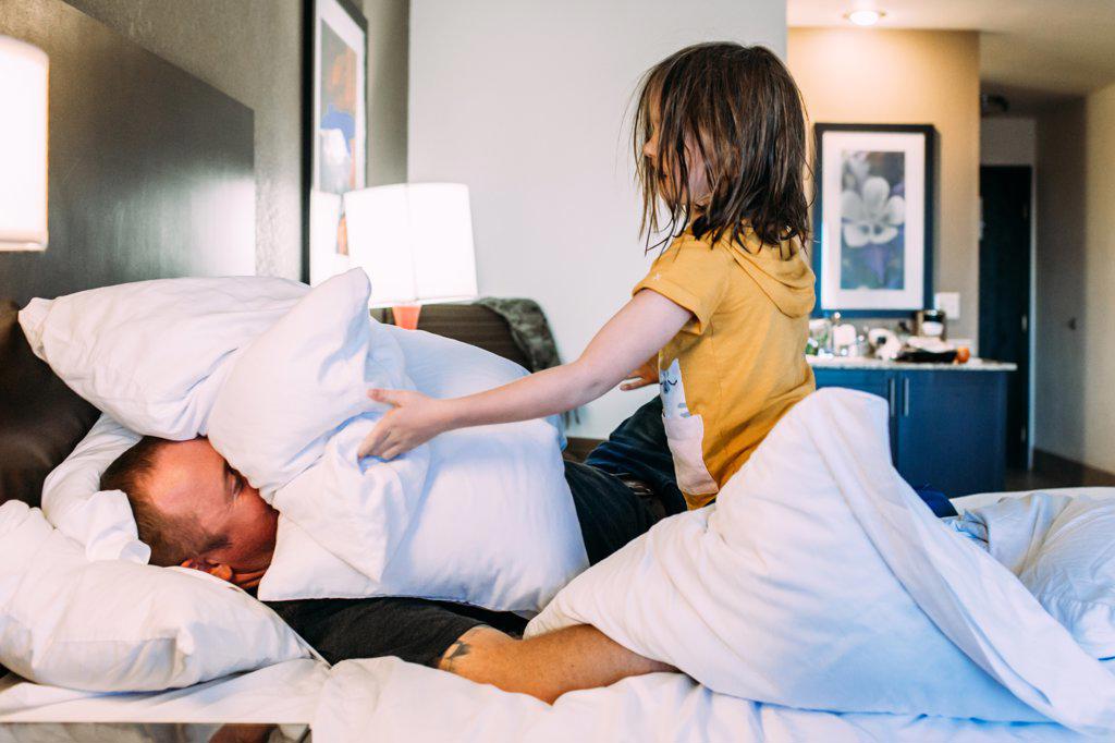 Happy young child playing with father on a bed in a hotel room