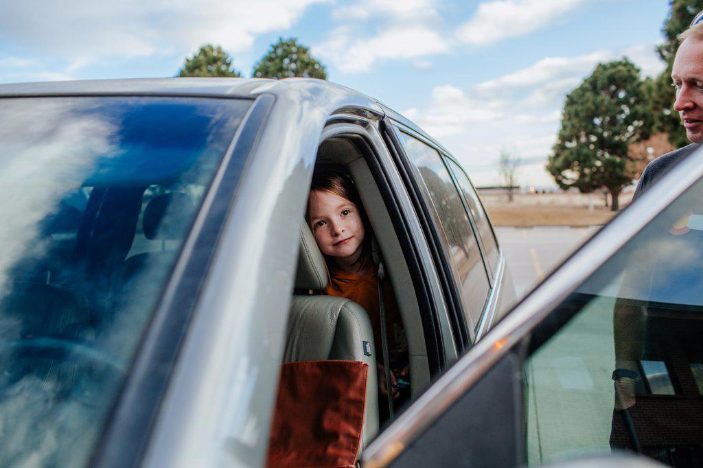 Young girl peeking out from back seat of a car before a trip