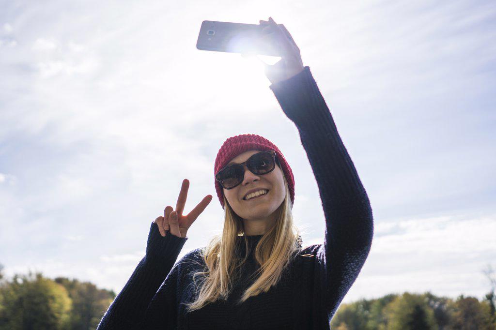 Canadian young woman in park using smartphone to take selfie