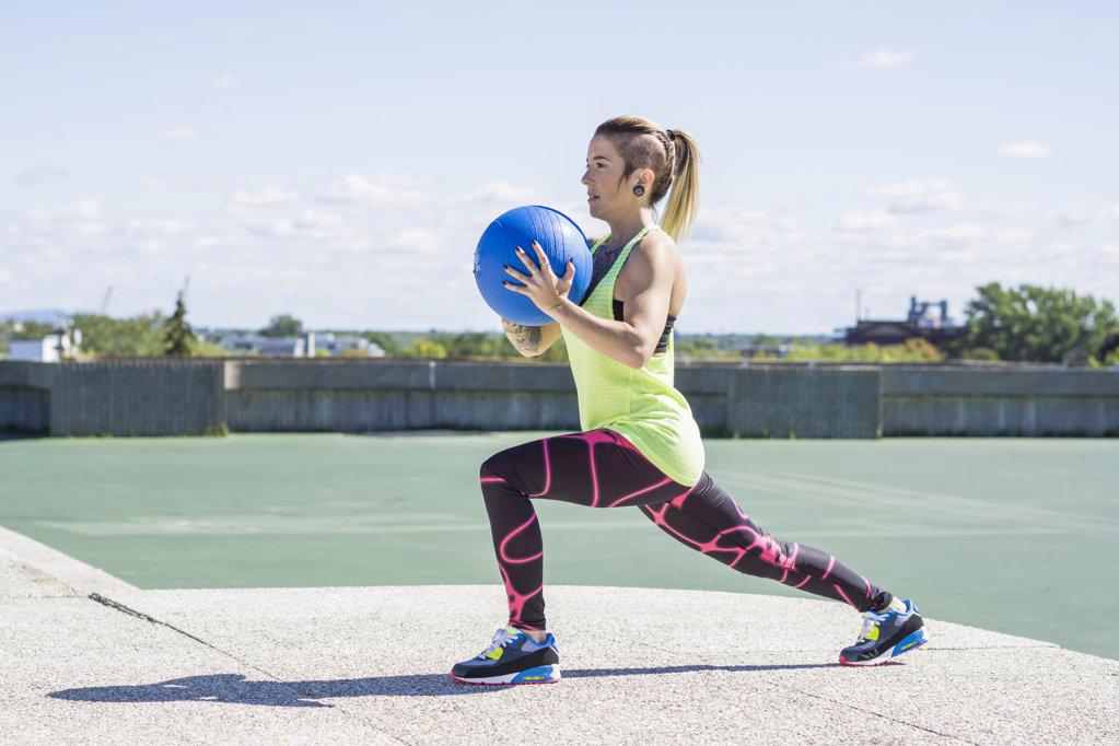 Female athlete working out with medicine ball on summer day