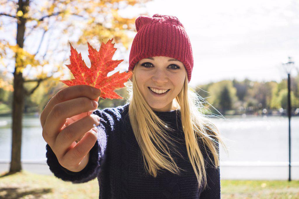 Female fashion model holding maple leaf towards camera