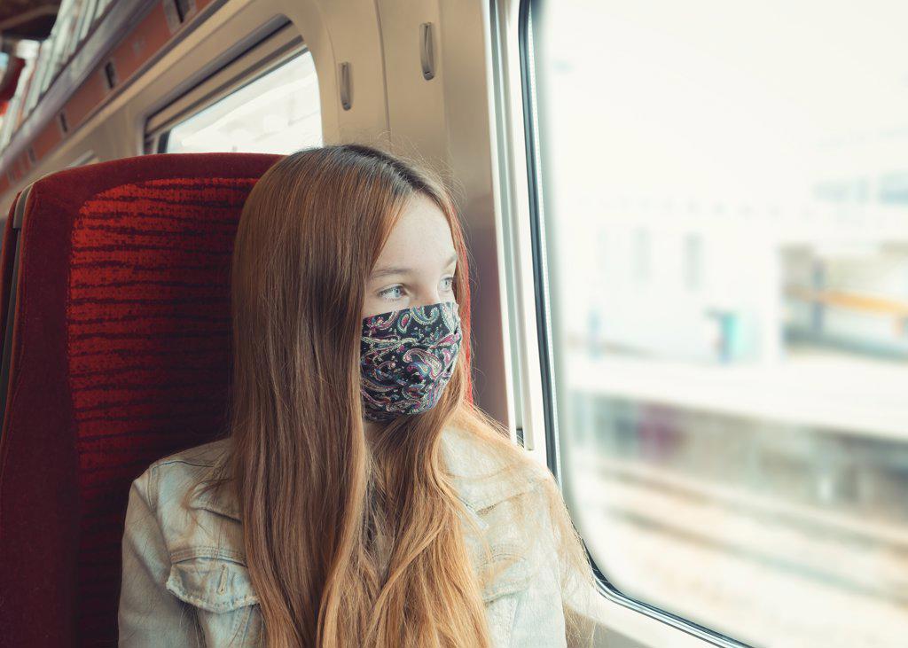 young teenager travelling on a train with mask looking out the window
